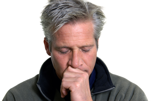 Mature man with gray hair looking concerned, hand to face, against white background.