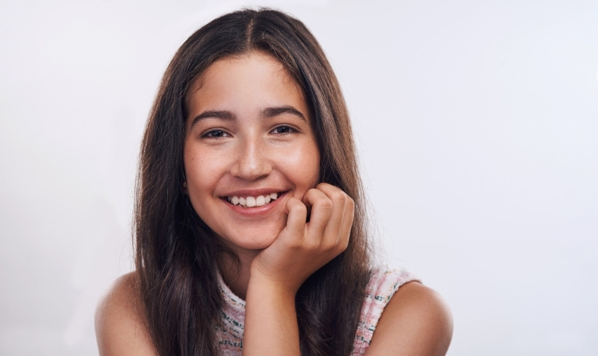 Young woman smiling at camera with hand on face against white background.