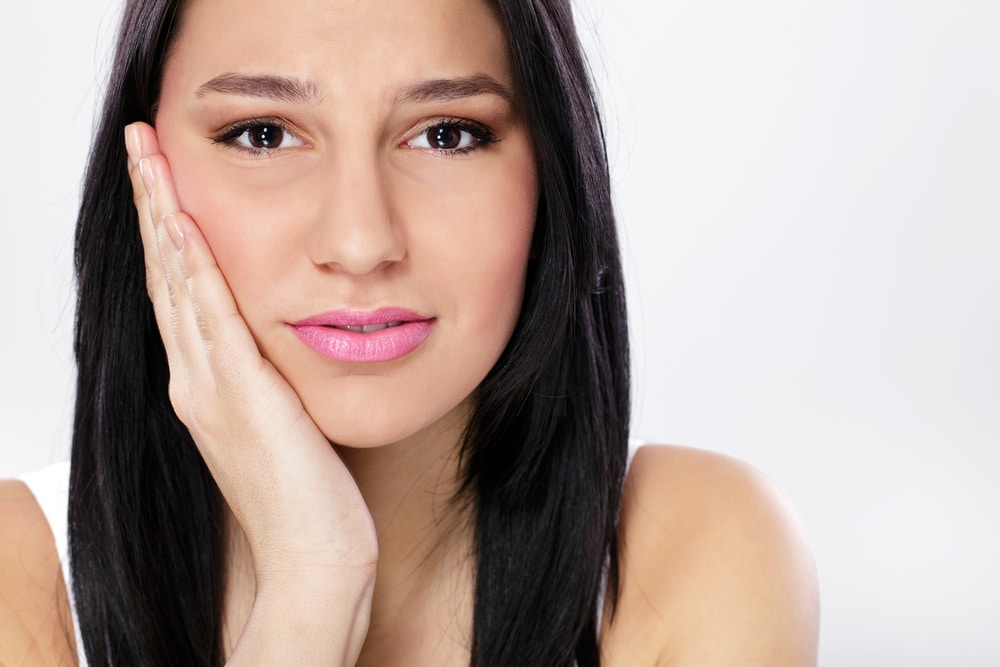 Woman touching her cheek with concerned expression, dental care portrait against white background.