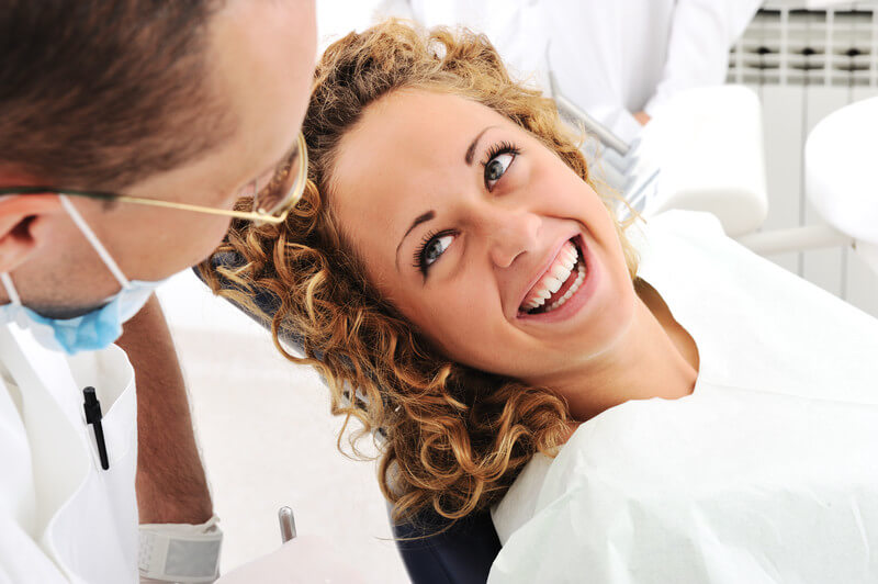 Dentist in white coat examining smiling patient in modern dental office setting.