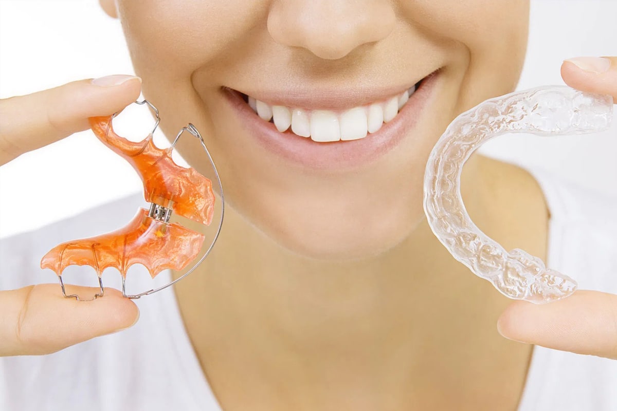 Woman smiling while holding orthodontic retainer and braces, displaying dental care products.