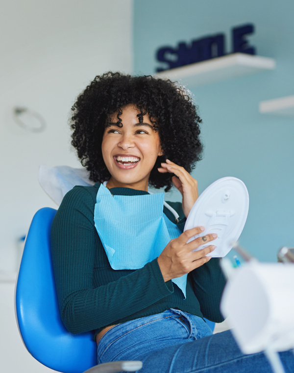 Smiling woman holding dental model in modern dental office setting.