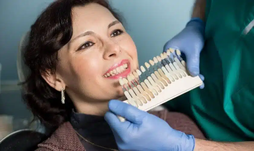 Woman holding dental shade guide during consultation at dental office, wearing blue gloves.