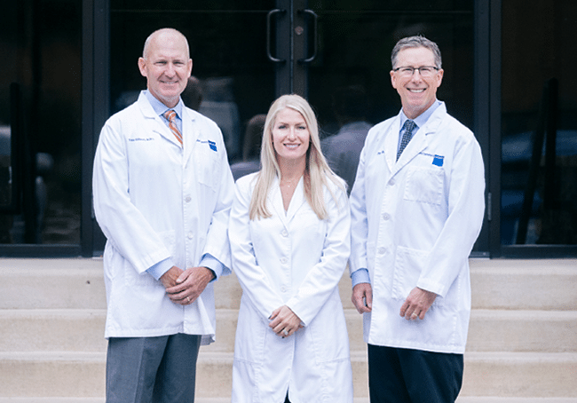 Three dental professionals in white coats standing together outside a modern clinic building.