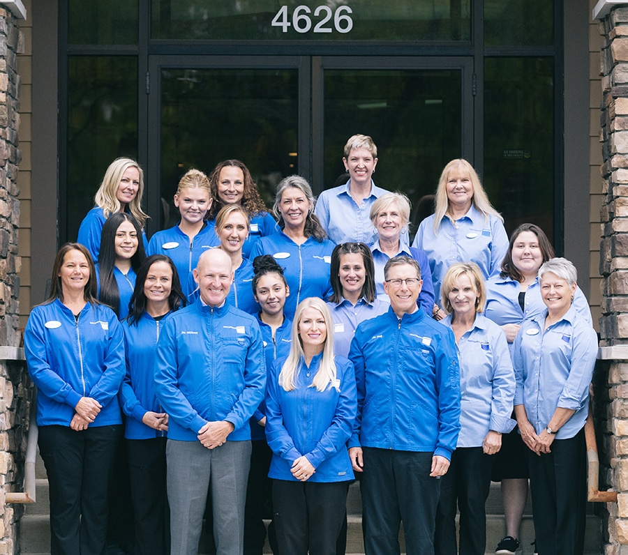 Team of dental professionals in blue scrubs posing outside clinic entrance at 4626.