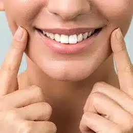 Young man smiling brightly while pointing to his teeth, demonstrating dental health and whiteness.