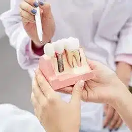 Dentist demonstrating dental implant model to patient in clinical setting
