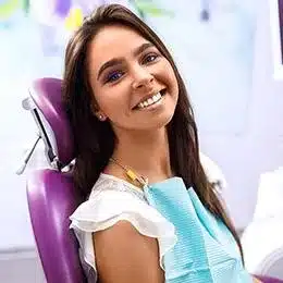 Young woman smiling in dental chair wearing purple bib at dentistry office.