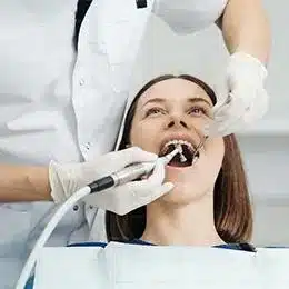 Woman receiving dental examination from dentist using instruments in clinical office setting.