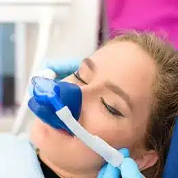 Young girl using blue asthma inhaler or dental aerosol device in clinical setting.