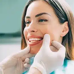 Woman smiling brightly while pointing to her teeth at the beach in dental care setting.
