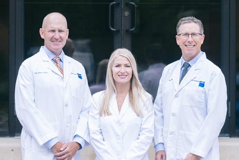Three dental professionals in white coats standing together outside a modern dental office entrance.